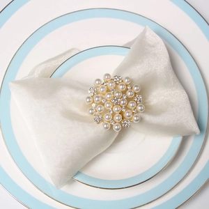 Elegant gold napkin ring with white pearls and rhinestones on a white plate set