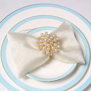 Golden flower napkin ring with pearls and rhinestones on a white silk napkin