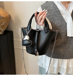Detail of black pebbled leather bucket bag with silver heart charm and metal chain strap