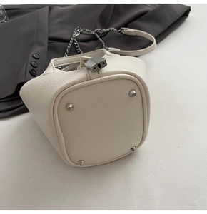 Detail of cream white pebbled leather bucket bag featuring silver hardware and protective feet