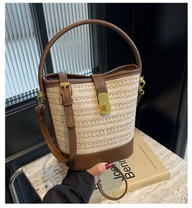 Detail of minimalist straw bucket bag with brown leather trim and golden metal clasp