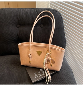 Détail d'un sac cabas rose mat avec logo triangulaire doré et breloque raquette de tennis