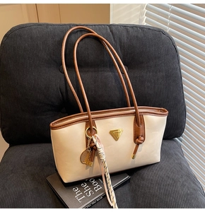 Détail d'un sac sous le bras beige avec pendentif raquette sur fauteuil velours