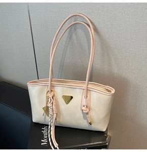 Détail du sac fourre-tout crème avec bordure rose, logo doré et breloque à pompon