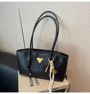 Détail du sac bandoulière en cuir noir avec breloques plume dorées et pompon tressé
