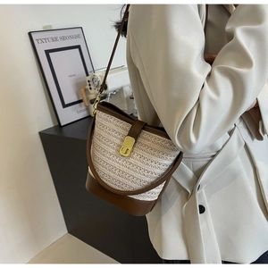 Detail of woven straw bucket bag with brown leather trim and golden twist lock clasp