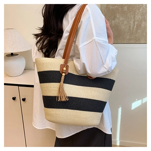 Détail du sac cabas en paille rayé avec anses en cuir marron et pendentif pompon