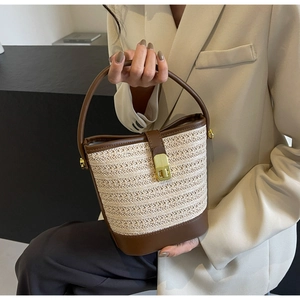 Detail of woven straw bucket bag with dark brown leather base and gold metal clasp