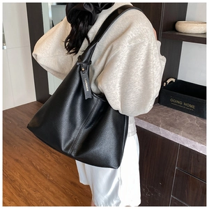 Close-up of black lychee texture leather tote bag with branded tag in indoor setting
