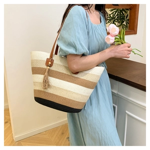 Détail du sac cabas en paille rayé avec anses en cuir marron et pompon décoratif