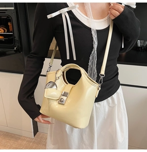 Detail of cream yellow leather bucket bag featuring a heart pendant and metal clasp