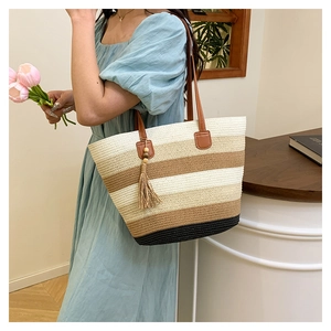 Détail du sac cabas en paille tissé à rayures avec anses en cuir et pompon décoratif