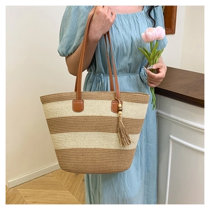 Détail du sac cabas en paille rayé avec anses en cuir marron et pompon en perles de bois