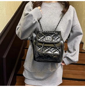 Detail of black quilted mini backpack with glossy finish and metal chain straps on model
