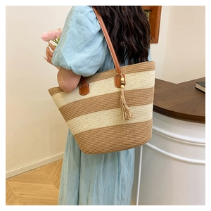 Détail d'un sac cabas en paille tissée avec anses en cuir brun et glands décoratifs