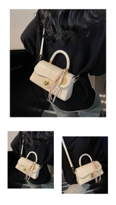 Détail du sac bandoulière crème avec fermoir rotatif doré et pompons décoratifs élégants