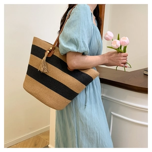 Détail d'un sac cabas en paille rayé avec poignées en cuir et pompon décoratif en bois