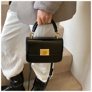 Detail of black leather handbag with braided handle and gold metal clasp worn on stairs