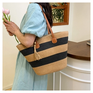 Détail du sac cabas en paille rayé avec anses en cuir marron et pompon décoratif