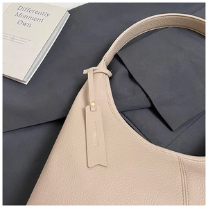 Detailed close-up of light beige litchi grain leather shoulder bag with brand logo tag
