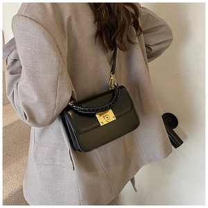 Detail of black leather handbag featuring woven handle and gold hardware on model