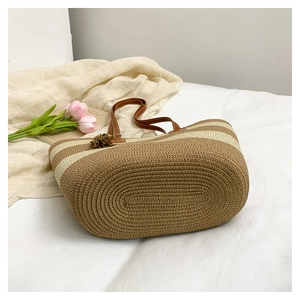 Détail d'un sac cabas en paille rayé avec poignées en cuir et breloque à pompon