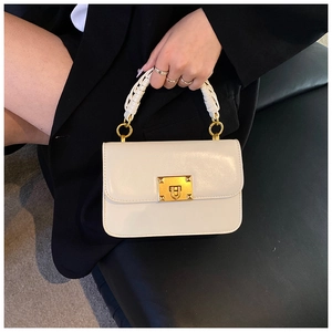 Detail of white square handbag with gold turn-lock and woven handle on dark background