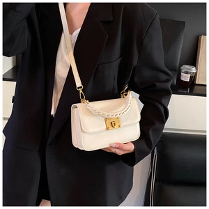 Detail of cream crossbody bag featuring a woven top handle and golden twist-lock closure