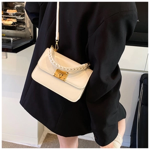 Close-up of cream square bag featuring a braided handle and gold-tone square lock detail