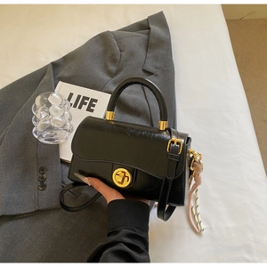 Détail du sac en cuir verni noir avec fermoir doré tournant et cordon tressé déco