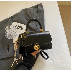 Détail du sac à main vintage en cuir noir avec fermoir doré et charme rayé élégant