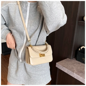Detail of a beige flap crossbody bag featuring a thick woven handle and gold metal lock
