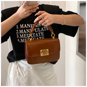 Detail view of brown leather handbag with woven handle and gold-tone twist lock