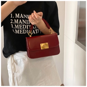 Detail of burgundy leather handbag featuring a gold square twist-lock and woven handle