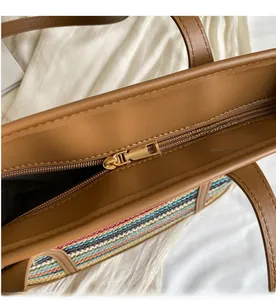 Detail of smooth gold zipper and brown leather trim on multi-color woven tote bag