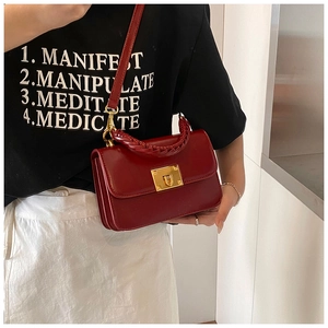 Close-up of wine red glossy leather handbag featuring woven handle and gold clasp