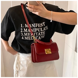 Détail d'un sac bandoulière en cuir rouge foncé avec poignée tressée et fermoir doré
