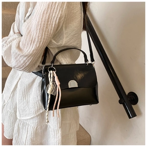 Detail of black glossy leather handbag featuring unique woven rope charms and metal buckle clasp