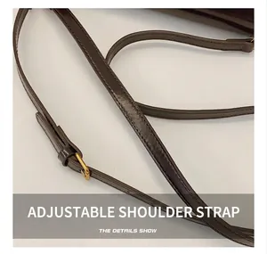 Détail d'une bandoulière en cuir marron avec boucle dorée et coutures précises