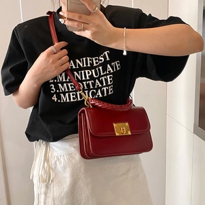 Fashionable dark red leather handbag with woven handle and gold twist lock in street style