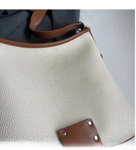 Close-up of creamy white pebble grain leather bag with brown trim and metal rivets