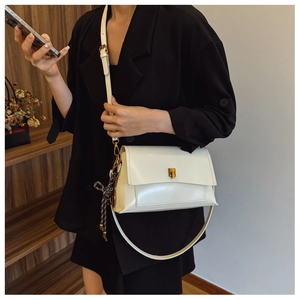 Détail d'un sac bandoulière en cuir crème avec fermoir doré et foulard à carreaux