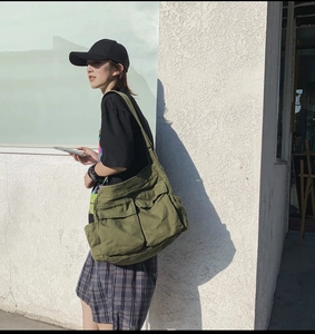 Side view of large army green canvas messenger bag worn by model in streetwear style