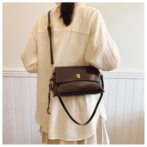 Détail du sac bandoulière en cuir ciré vintage avec fermoir doré sur fond de mur blanc