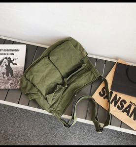 Flat lay detail of an army green canvas shoulder bag with multi-pocket utility design