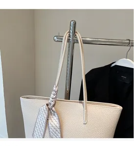 Close-up of beige tote bag handle featuring a decorative geometric silk scarf wrap