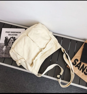 Detail view of cream canvas messenger bag with large front pockets and black buckles