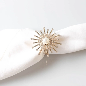 Detail of gold flower napkin ring with center pearl and radiant rhinestones on white linen