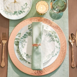 Detail of rose gold hammered napkin ring on sage green fabric with floral tableware