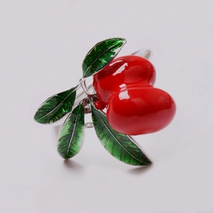 Vista macro de anillo de fruta roja artificial con hojas verdes brillantes sobre plata